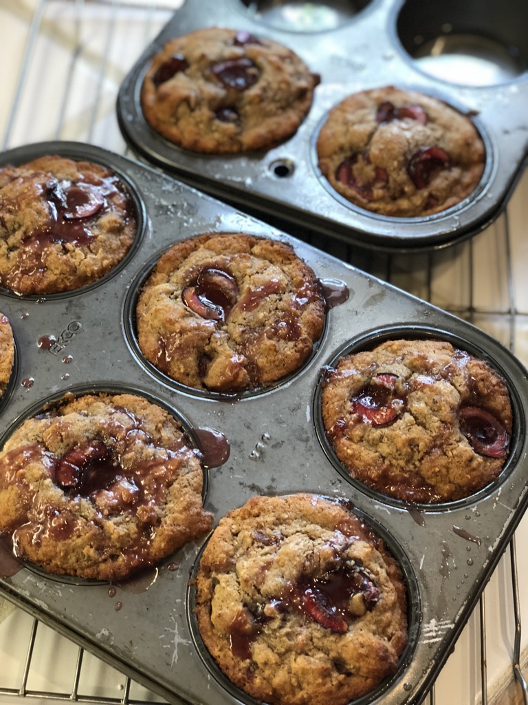 close up of freshly baked cherry muffins in metal tins sitting on cooling rack in kitchen with white counter top