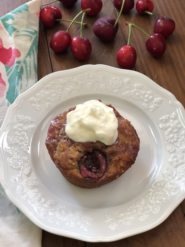 finished cherry muffin on white plate with topping and fresh cherries for color