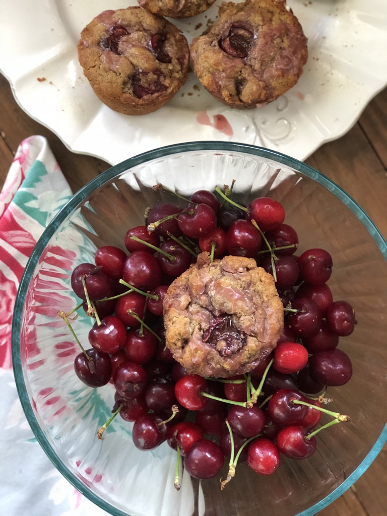 gluten free cherry muffins together on plate. one cherry muffin in clear glass bowl sitting on top of fresh cherries.