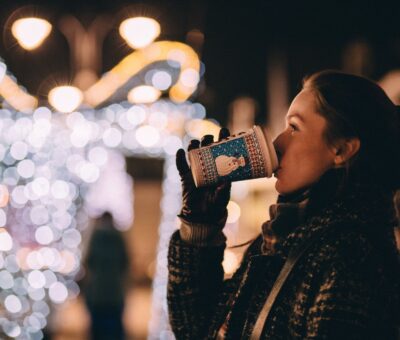 woman drinking coffee outside with holiday lights