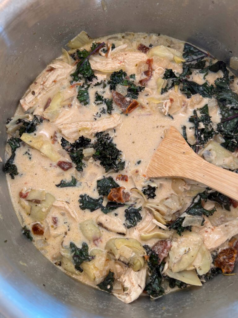 tuscan chicken soup cooking in pot with wooden spoon